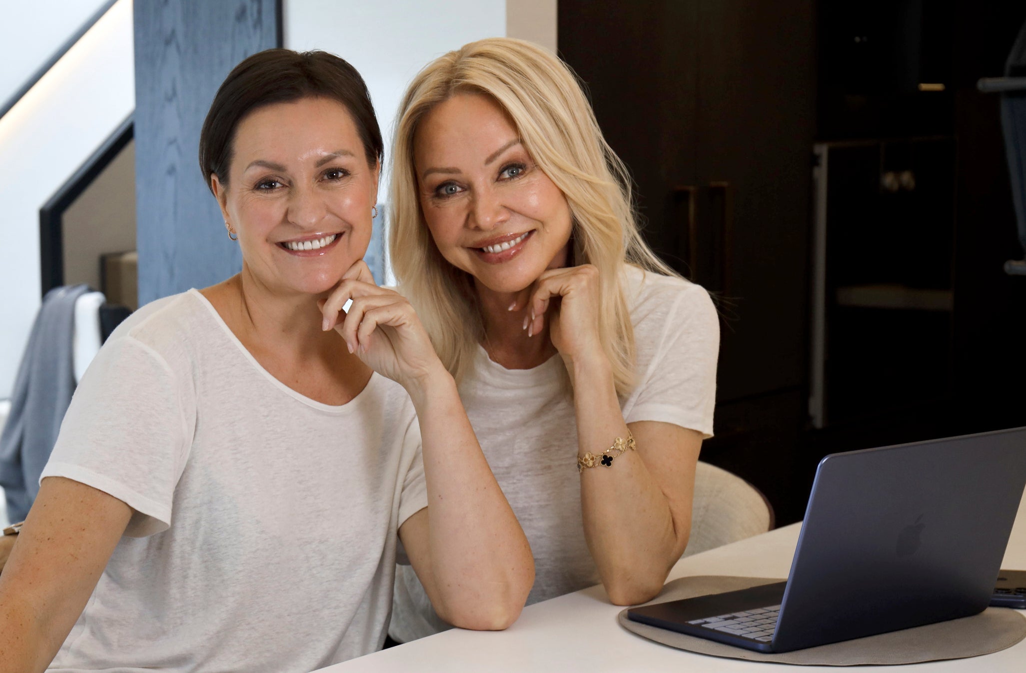 Linda Johansen og May Britt smiler ved et bord med en bærbar PC